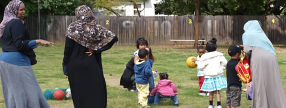 Young children playing together on grass with mums nearby